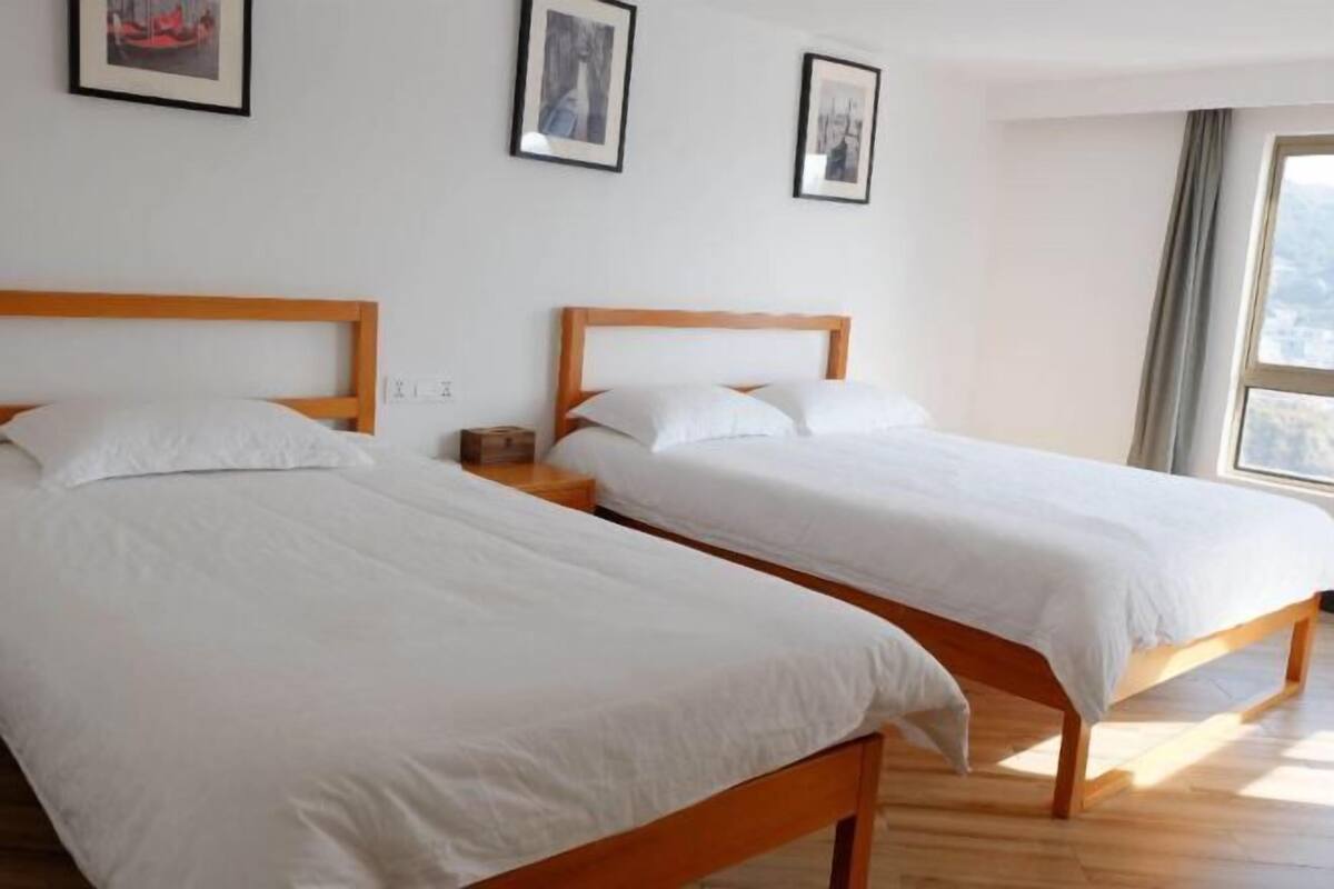 Ein Zimmer mit zwei hölzernen Betten, weißer Bettwäsche, einem Nachttisch und gerahmten Bildern an der Wand.