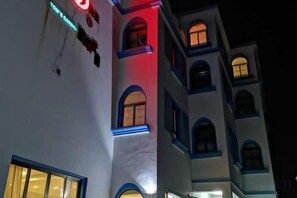Un immeuble à plusieurs étages, avec des fenêtres illuminées et un panneau lumineux au néon.