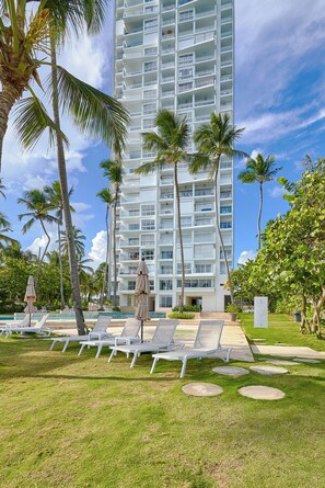 Um hotel moderno com área de piscina, espreguiçadeiras e palmeiras.