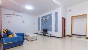Ein Wohnzimmer mit einem blauen Sofa, einem weißen Couchtisch, einem Flachbildfernseher und einem Wandkunstwerk.