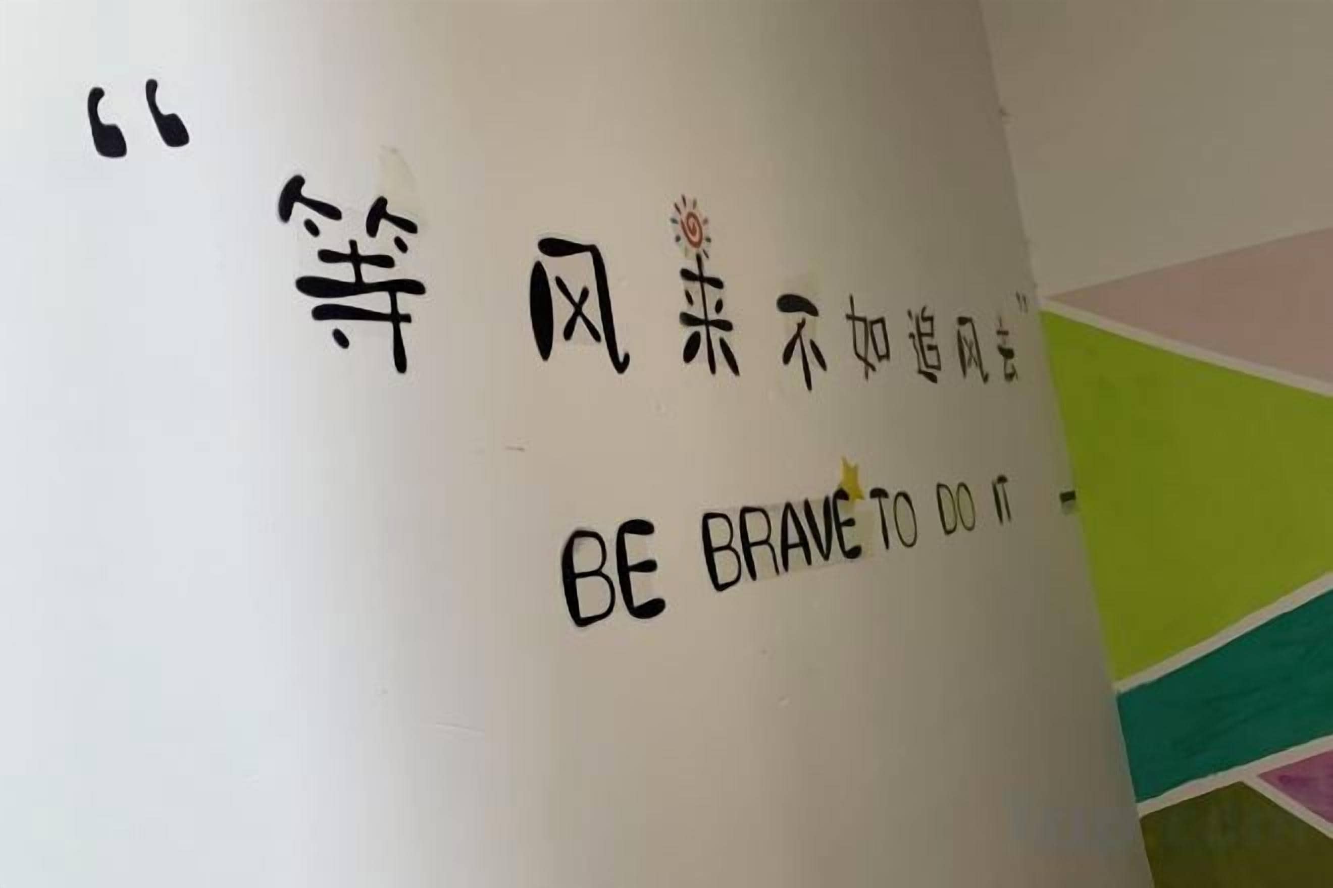 A wall with a quote in Chinese characters and its English translation 'BE BRAVE TO DO IT'.