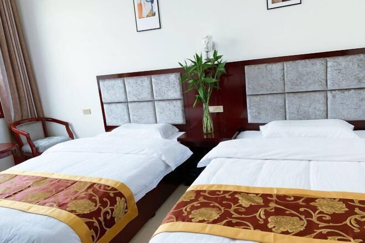 A hotel room with two beds, a wooden headboard, a nightstand with a vase of flowers, and a chair.