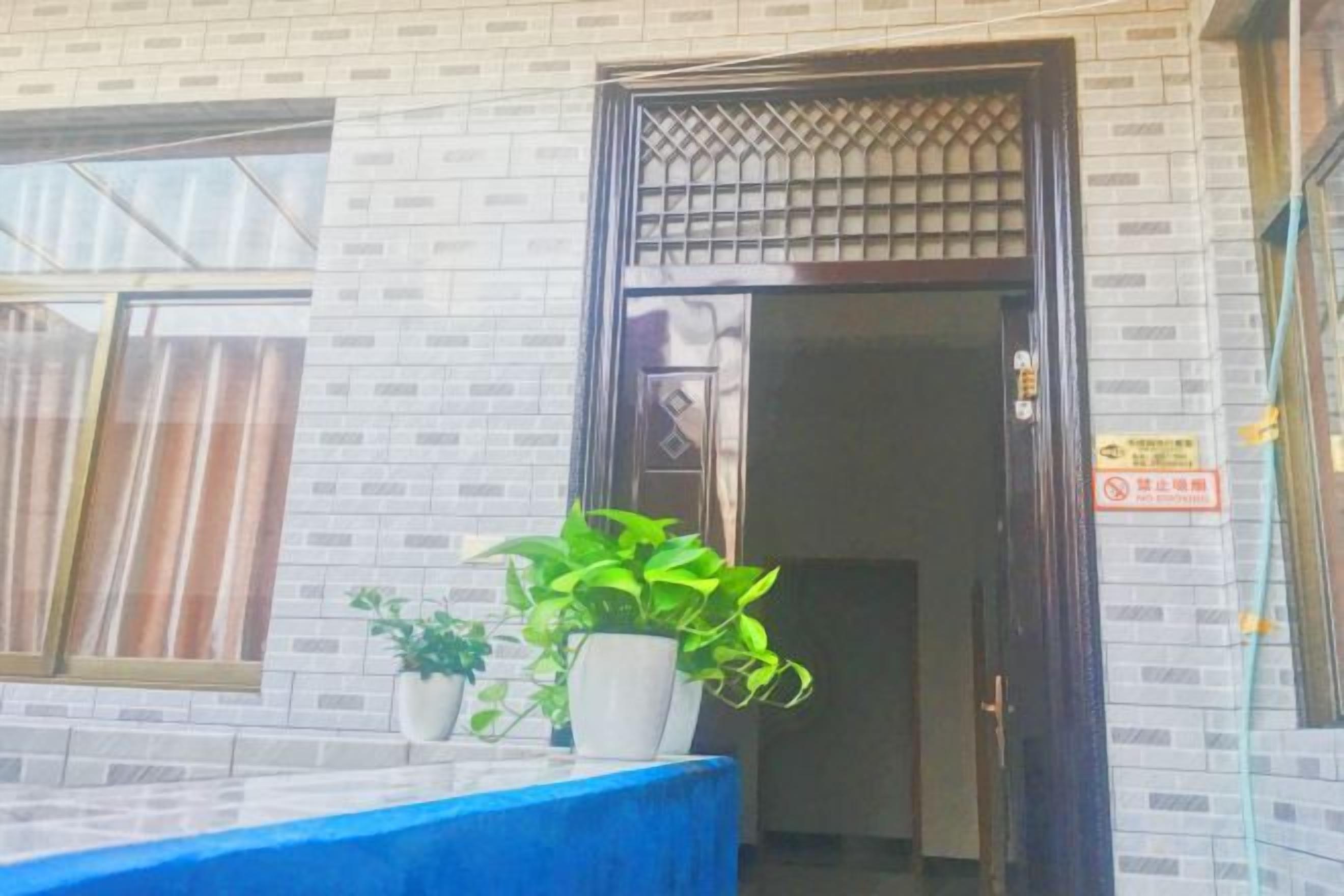 A building entrance with a tiled facade, a potted plant, and a blue table.