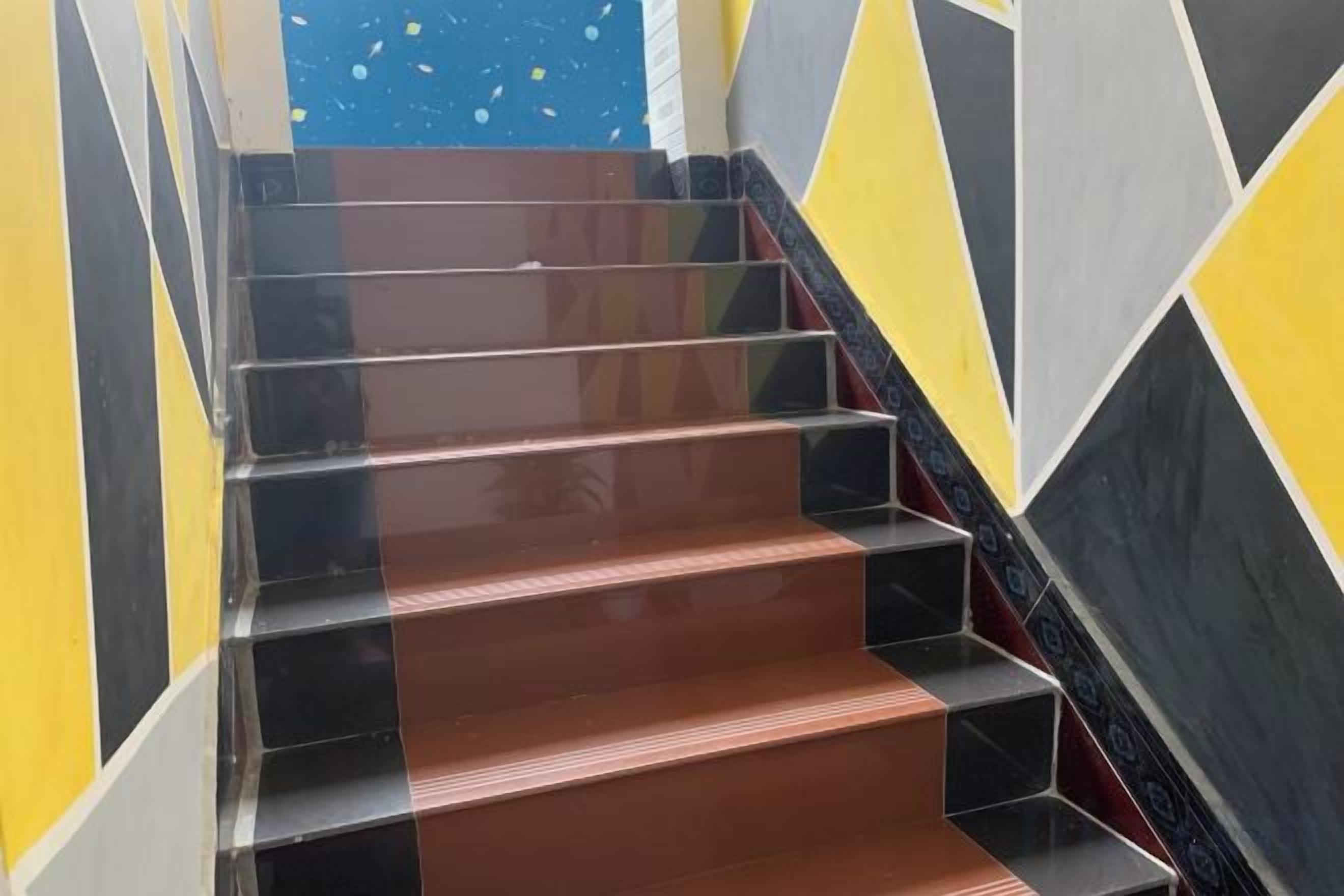 A staircase with alternating black and brown steps, surrounded by walls with geometric patterns.
