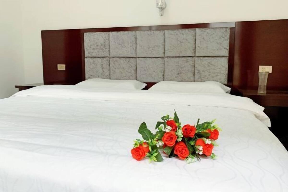 A hotel room with a large bed, a headboard with a grey panel design, and a nightstand with a vase of flowers.
