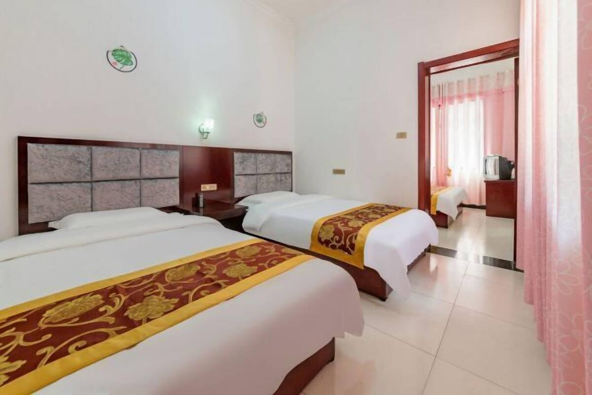 A hotel room with two beds, a wooden headboard, a nightstand, and a door leading to another room.