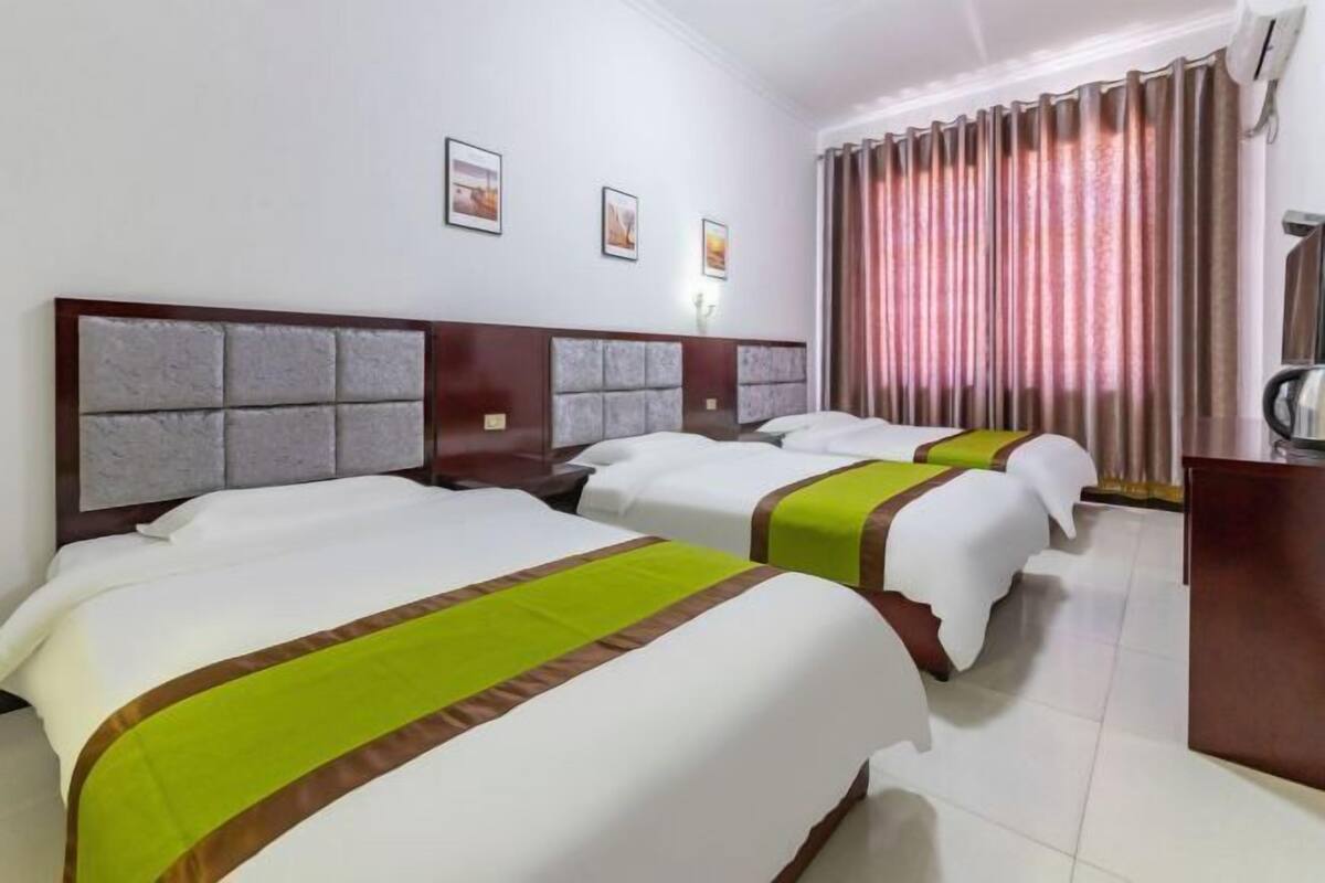 A hotel room with three beds, a desk, and a large window with curtains.