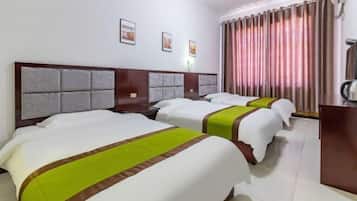 Habitación de hotel con tres camas, un escritorio y un ventanal grande con cortinas.