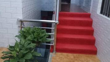 A staircase with red carpeted steps and a metal handrail, leading to an upper floor.