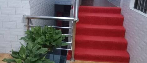 Eine Treppe mit roten Teppichstufen und einem Metallgeländer, die zu einer oberen Etage führt.