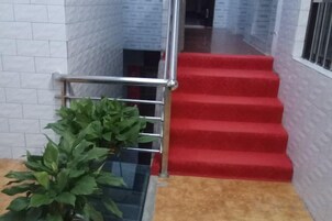Una escalera con peldaños alfombrados en rojo y barandilla de metal, que conduce a un piso superior.