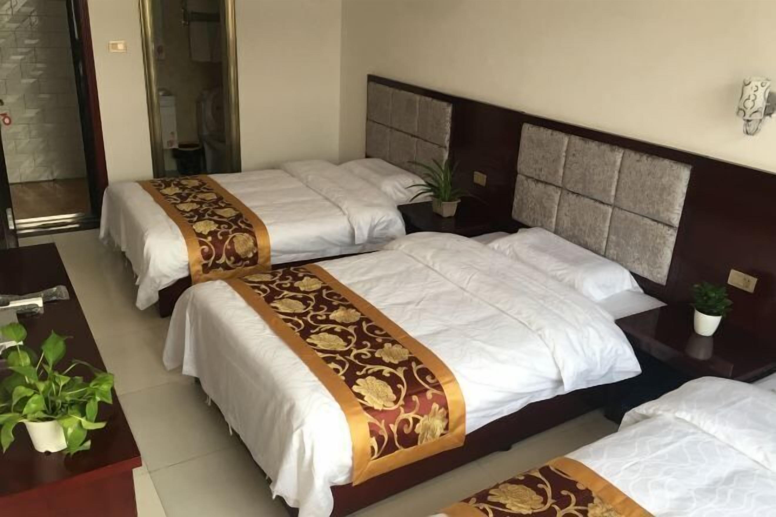 A hotel room with two beds, a desk, and a potted plant.