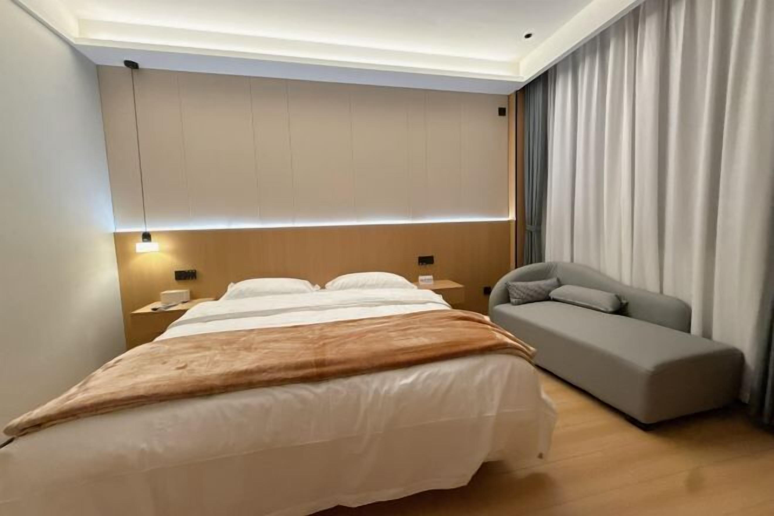 A hotel room with a bed, bedside tables, a sofa, and a curtain.