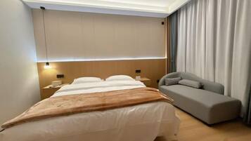 A hotel room with a bed, bedside tables, a sofa, and a curtain.