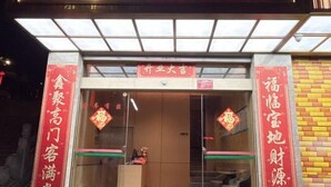 Entrada de un hotel con mostrador de recepción, puertas de cristal y caracteres chinos en las paredes.