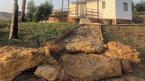 A single-story mobile home with a covered porch, surrounded by a garden with palm trees and a rocky terrain. - Vacation homes Trinacria (Sicilia)