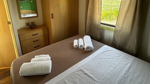 A bedroom with a bed, a wooden wardrobe, a mirror, a window with curtains, and a view of a green landscape. - Vacation homes Trinacria (Sicilia)
