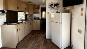 A compact kitchen with wooden cabinets, a white refrigerator, and a wall-mounted TV. - Vacation homes Trinacria (Sicilia)