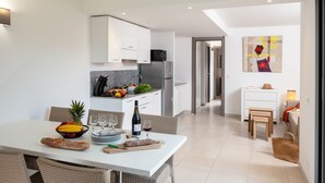A modern kitchen with white cabinets, a dining area with wicker chairs, and a view into the living room. - MB6 Loggia by Interhome (Moriani-Plage)