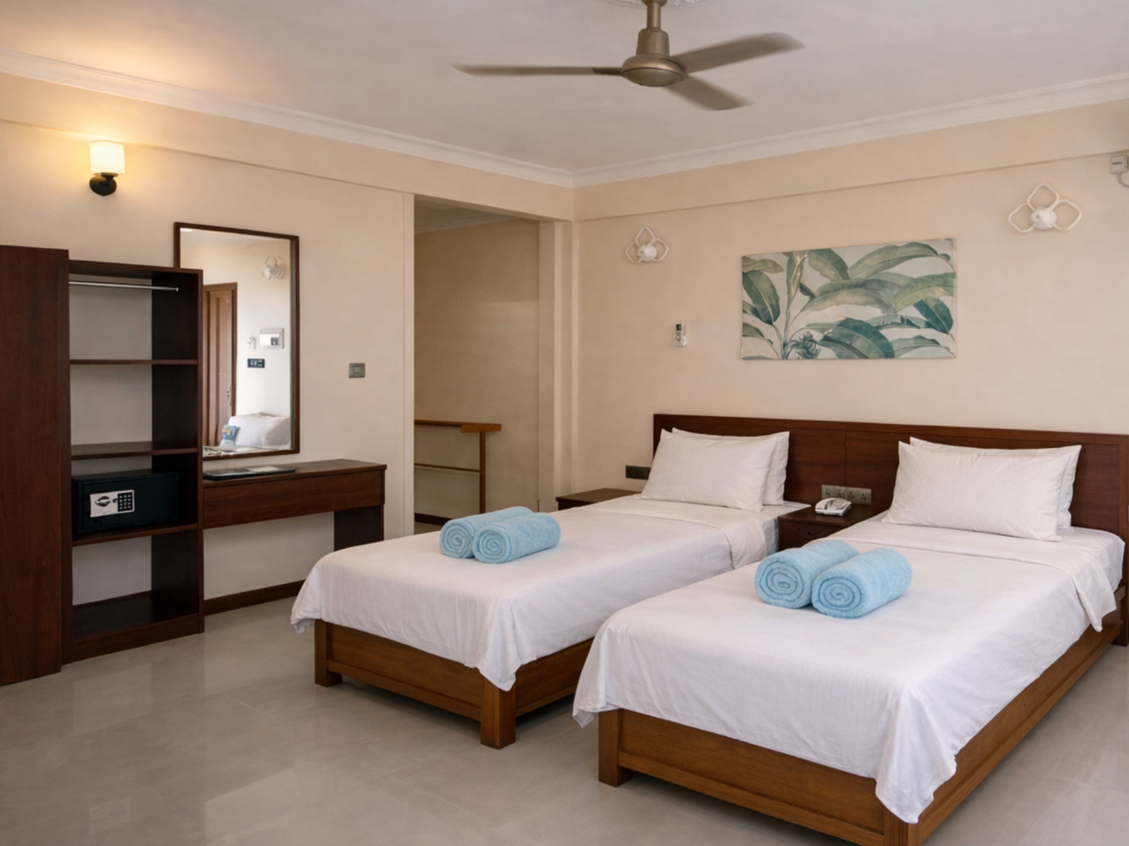A hotel room with two beds, a desk, a mirror, and a ceiling fan.