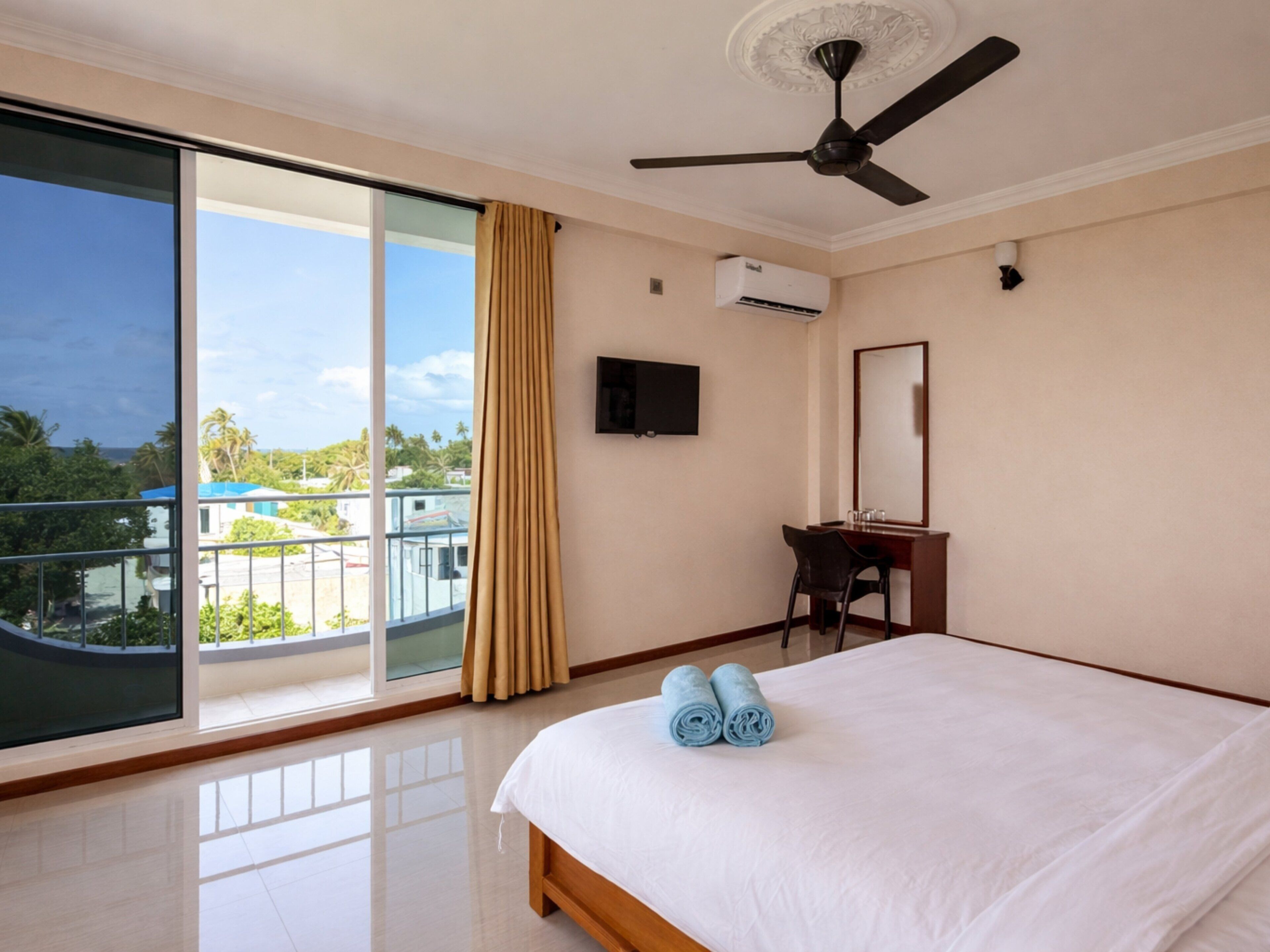 Habitación de hotel con cama, escritorio, silla, televisor y balcón con vistas.