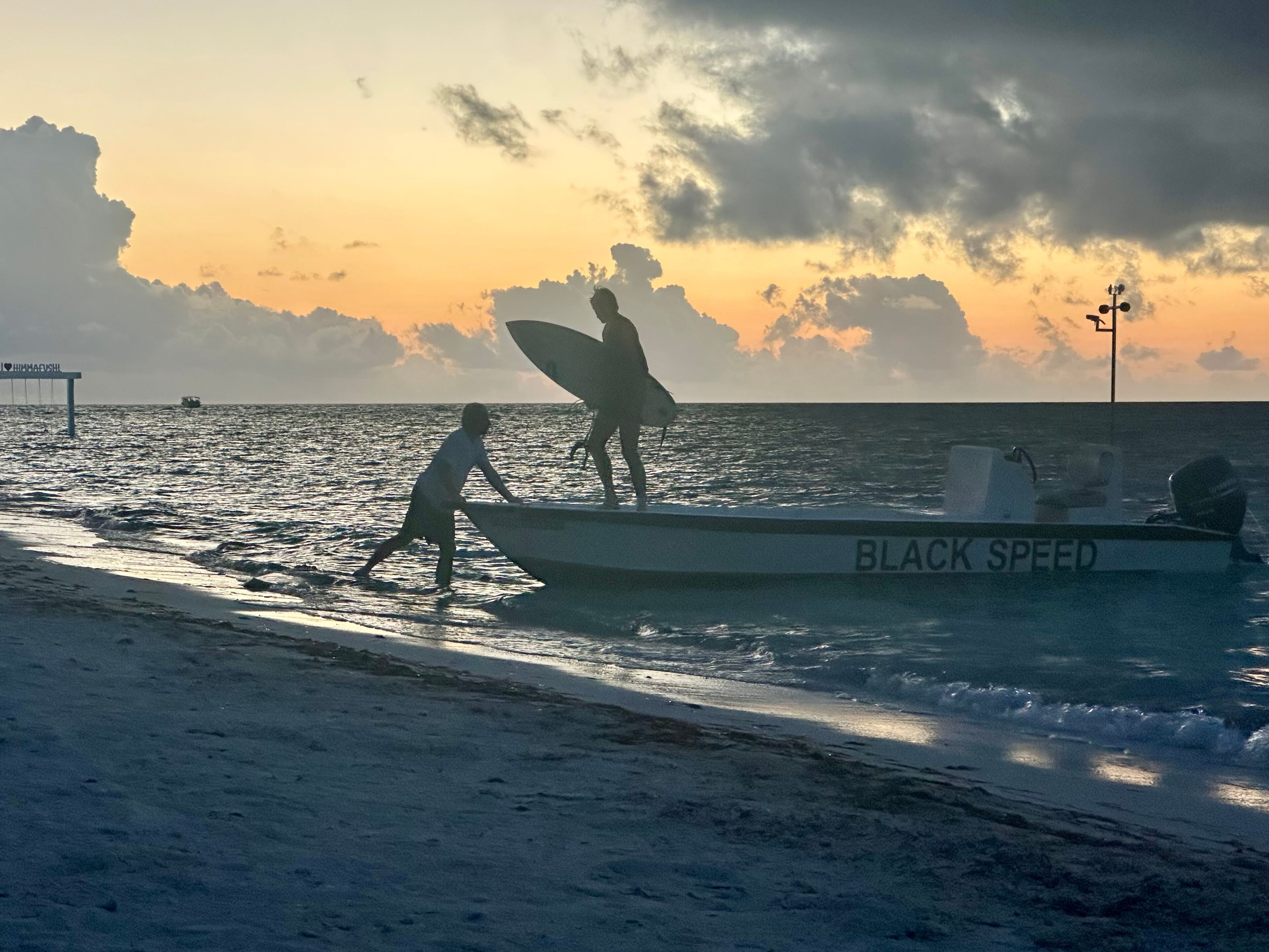 Un bote llamado BLACK SPEED en una playa con un atardecer de fondo.
