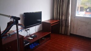 A room with a flat-screen TV mounted on the wall, a wooden desk, a chair, and a window with curtains. - Xing'an Hongfu Business Hotel (Xing'an County)