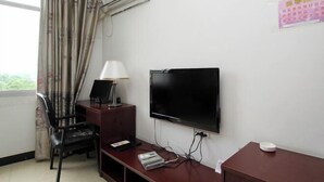 Habitación de hotel con televisión, escritorio con lámpara, una silla y ventana con cortinas.