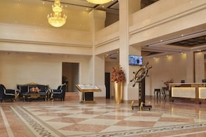 A hotel lobby with a check-in counter, seating area, and a chandelier.