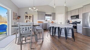 Une cuisine moderne avec des meubles gris, un îlot central, des tabourets de bar et un coin repas comprenant un banc et des chaises.