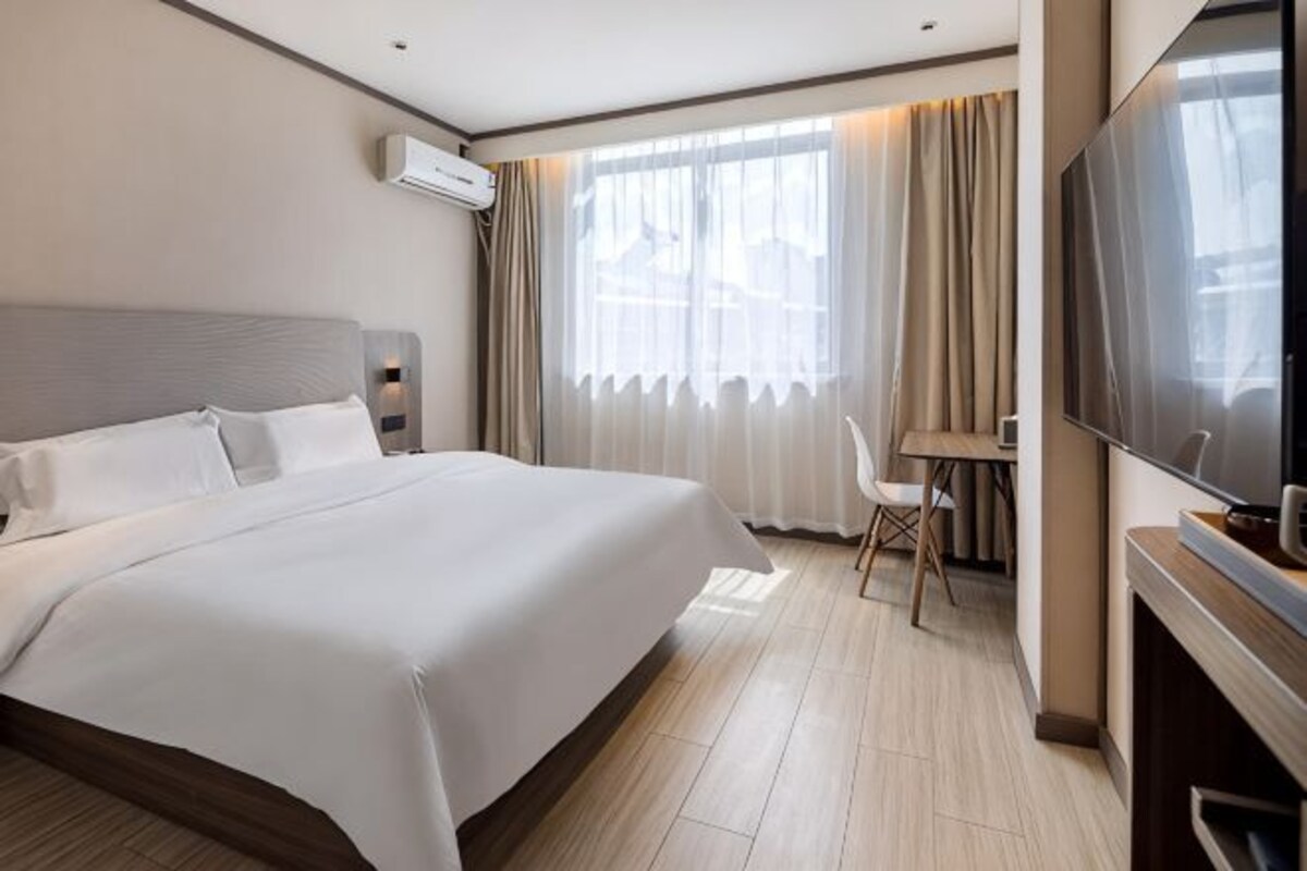 A hotel room with a large bed, a desk with a chair, a flat-screen TV, and a fireplace.