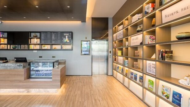 Un hall d’hôtel moderne comprenant un comptoir d’accueil, un écran numérique affichant le menu et une bibliothèque contenant divers ouvrages.