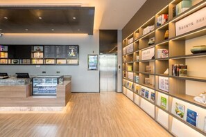 A modern hotel lobby with a reception desk, a digital menu board, and a bookshelf with various items. - HanTing Hotel (Hai'an Wenfeng Great World) (Hai'an)