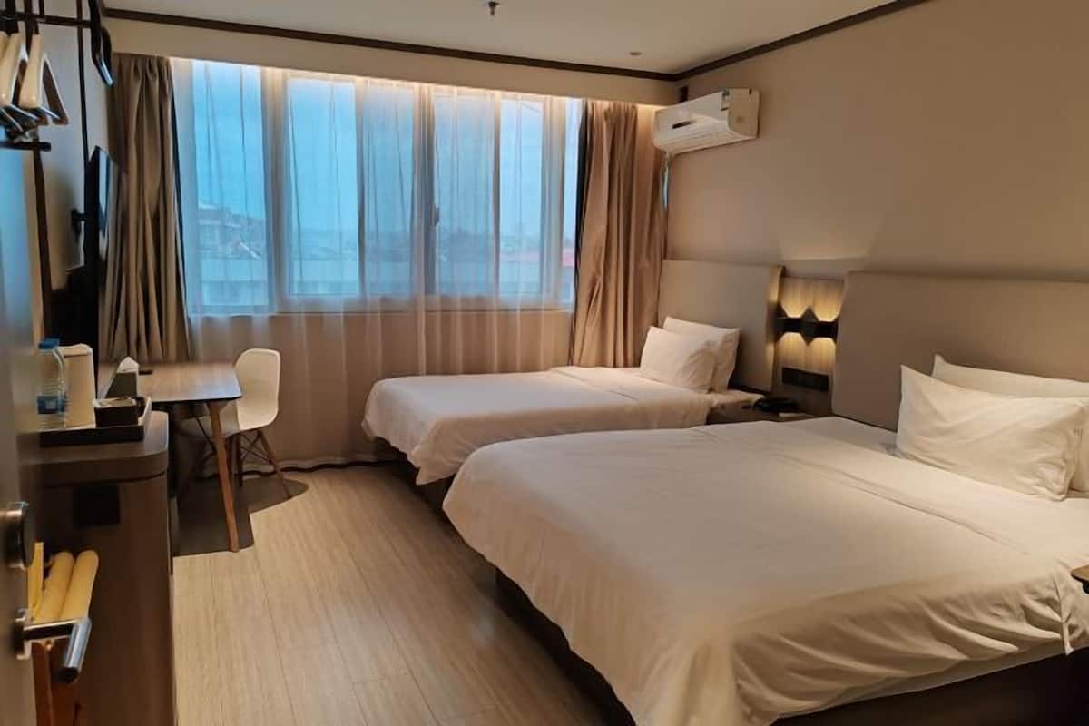 A hotel room with two beds, a desk, a chair, and a large window with curtains.