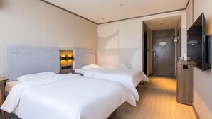 Une chambre d’hôtel avec deux lits, une télévision et une salle de bain visible à travers une porte ouverte.