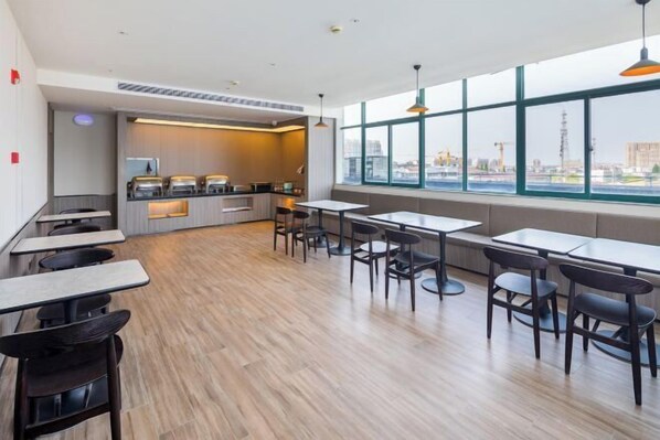 A modern restaurant with a long counter, multiple tables, and chairs. There is a kitchen area with appliances visible. Large windows provide a view of the cityscape. - HanTing Hotel (Hai'an Wenfeng Great World) (Hai'an)