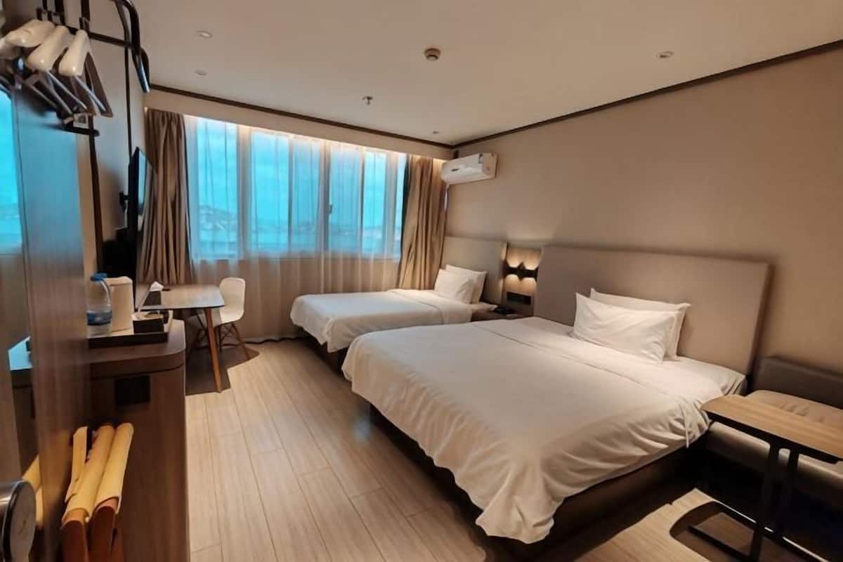 A hotel room with two beds, a desk, a chair, and a window with curtains.