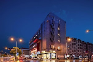 Un edificio de varios pisos con una planta baja comercial, entrada visible y vista a la calle con semáforos y vehículos.
