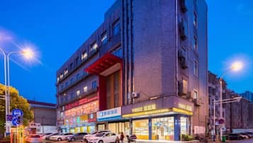 A multi-story building with commercial spaces on the ground floor, including a brightly lit storefront and a parking area with cars.