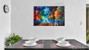 Zona pranzo con tavolo apparecchiato per quattro persone, un quadro colorato appeso al muro, una sveglia e una pianta in vaso.