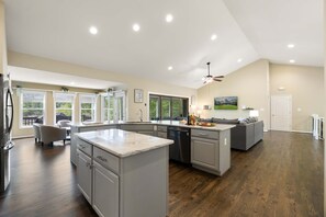 Una cocina amplia con una isla grande, electrodomésticos integrados y un comedor con sofá gris.