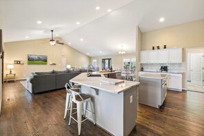 A spacious living area with a large gray sectional sofa, a kitchen with white cabinets, and a dining area with a table and chairs.
