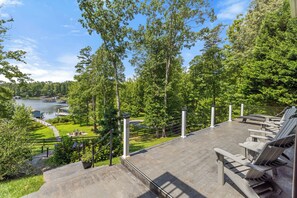 A deck with Adirondack chairs overlooking a lake and forest.
