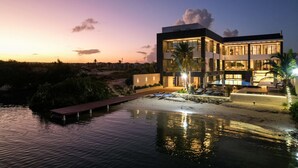 A modern multi-story building with a pool, surrounded by water and vegetation.