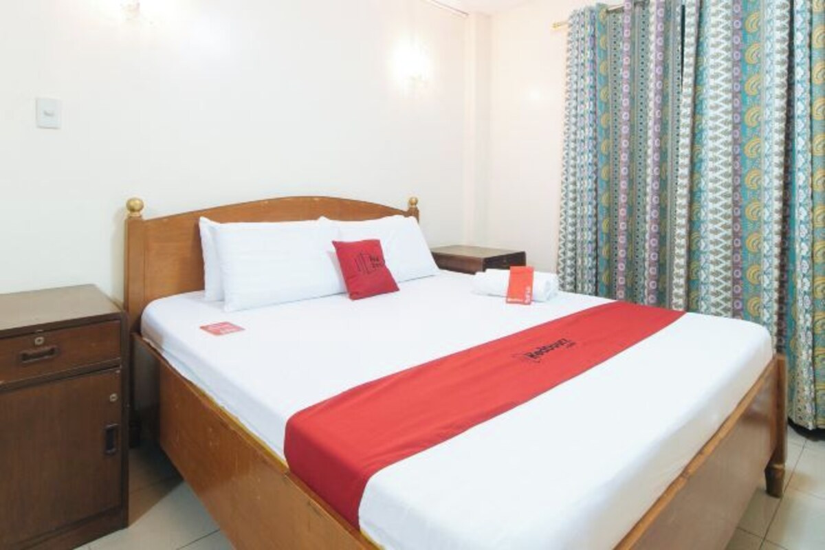 A neatly made bed with a red blanket, a wooden headboard, and a white pillow.