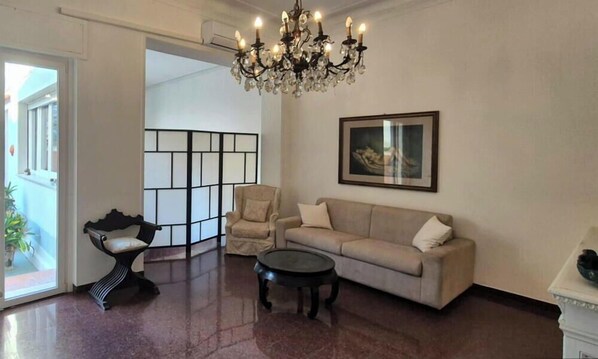 Ein Wohnzimmer mit einem Kronleuchter, einem Sofa, einem Sessel, einem Couchtisch und einem gerahmten Bild an der Wand.