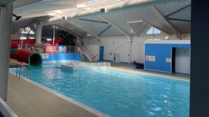 An indoor swimming pool with a slide, a lifeguard stand, and a blue restroom sign. - Paws a While! caravan with uninterrupted views of Solent and direct beach access (Great Thorness)