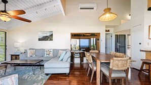 A spacious living room with a grey sofa, wooden dining table, and woven chairs. - 180 Degree Ocean View in Wailea! WE204 (Kihei)