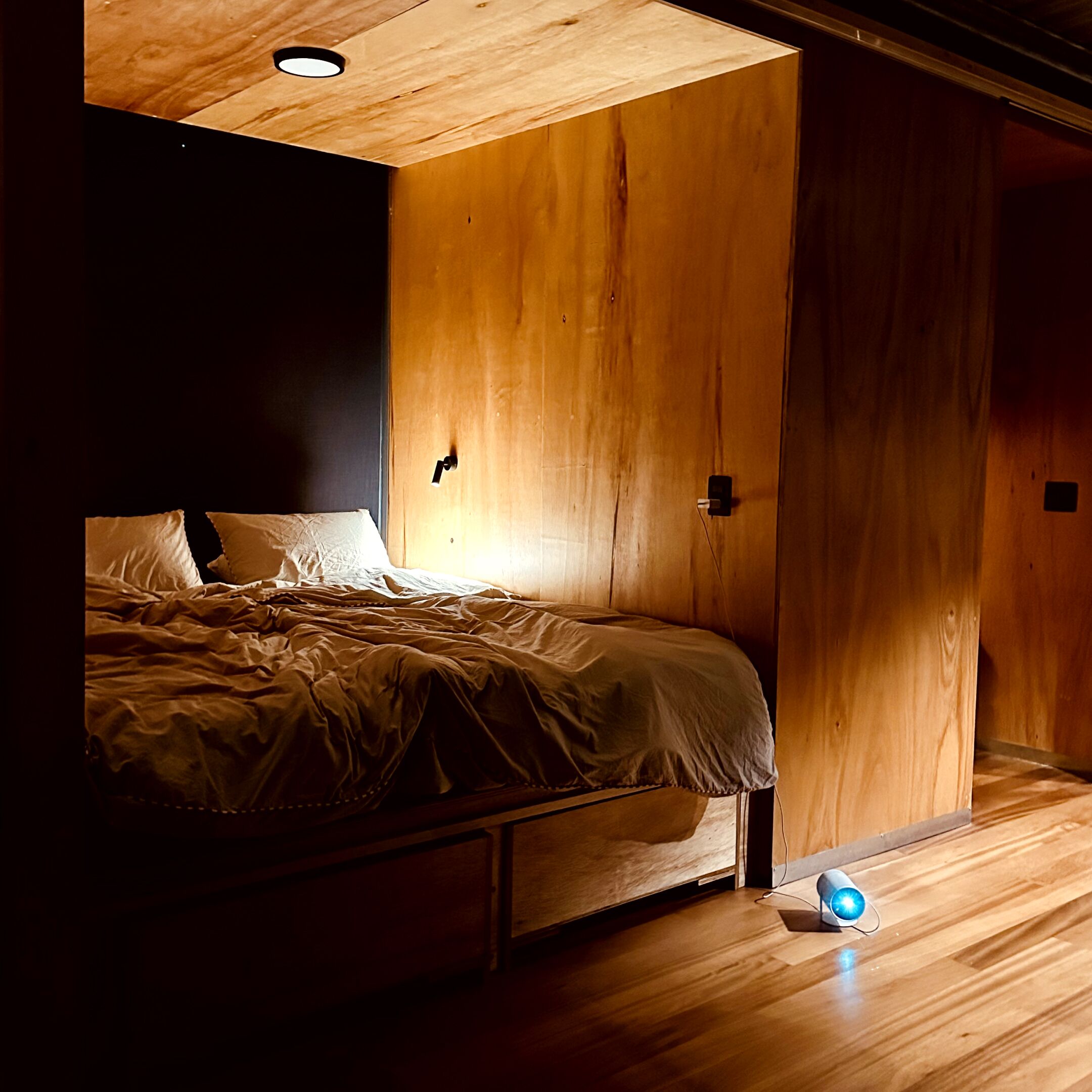 Ein Schlafzimmer mit Holzboden, einem Bett, einem Nachttisch und einer Wandleuchte.