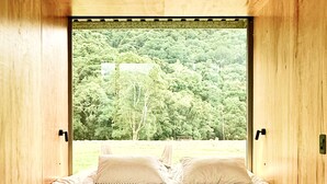 Ein Schlafzimmer mit großem Fenster, Holzwänden und einem Bett mit Kissen.